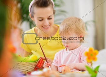 Mom helping baby painting on Easter eggs