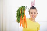 Smiling woman in rabbit ears showing bunch of carrots