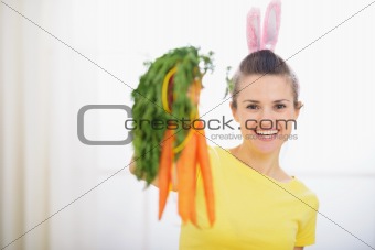 Smiling woman in rabbit ears showing bunch of carrots