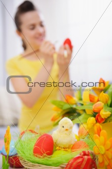 Closeup on basket of Easter eggs and woman painting on egg in background