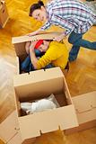 Smiling girl trying to pack boyfriend in cardboard box