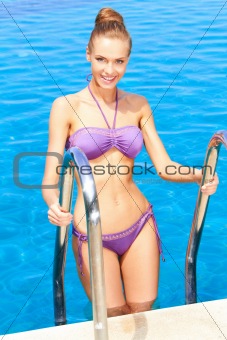 Cute woman standing on pool ladder