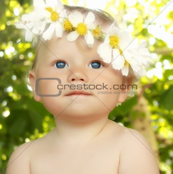 Smiling baby in a flower wreath in green summer background