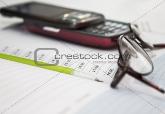 Pen, mobile phone and glasses in composition on a notebook