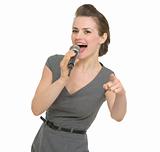 Happy woman singing in microphone and pointing on you isolated