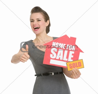 Happy realtor with home for sale sold sign showing thumbs up isolated