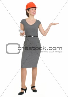 Full length portrait of happy architect woman showing something on empty hand isolated
