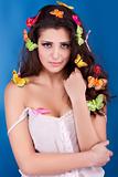Beautiful girl with butterflies in hair poses in studio isolated on blue
