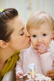 Mother kissing baby eating birthday cake
