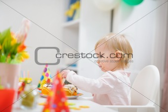 Baby sitting at table and eating birthday cake