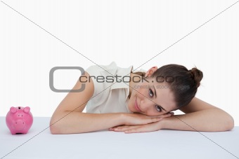 Businesswoman leaning on her desk with a piggy bank