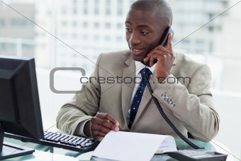 Smiling entrepreneur making a phone call while looking at his computer