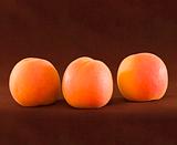 Three Ripe Organic Apricots On Brown Backround
