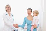 Happy mother holding baby and shaking hand to pediatric doctor