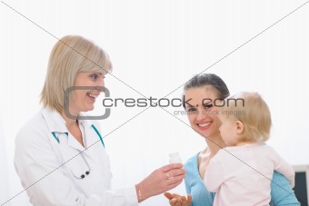 Middle age pediatric doctor giving pills bottle to mother with baby