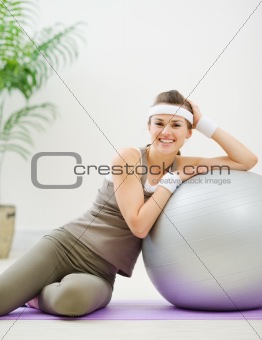 Happy woman sitting near fitness ball