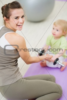 Baby helping mother lifting dumb-bell