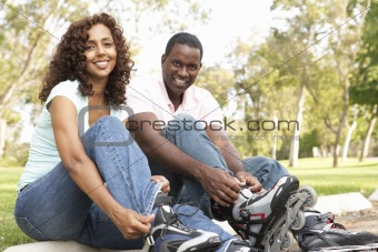 Couple Putting On In Line Skates In Park