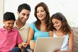 Family Sitting On Sofa At Home With Laptop