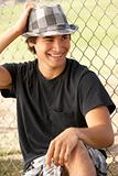 Teenage Boy Sitting In Playground Wearing Hat
