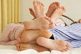 Close Up Of Family's Feet Relaxing On Bed At Home