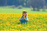 boy with long blond hair picking dandelions in a field smiling