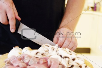 Man is cutting meat and mushrooms