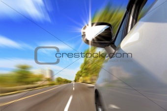 car on the road with motion blur and sunlight in the mirror