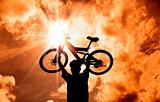 The Silhouette of mountain biker raised bicycle with sunset and cloud background