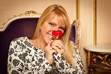 Seated Beautiful Blonde Woman Smiling While Smelling Red Rose.