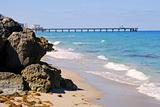 Scenic view of rocky beach by blue sea with long pier in background, Florida, U.S.A.