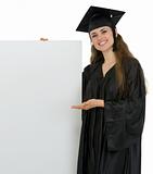 Smiling graduation student woman showing on blank billboard
