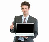 Modern businessman showing laptops blank screen and thumbs up