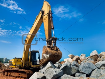 Yellow tracked excavator with rock