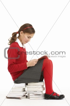 Female Student In Uniform Sitting On Pile Of Books Reading