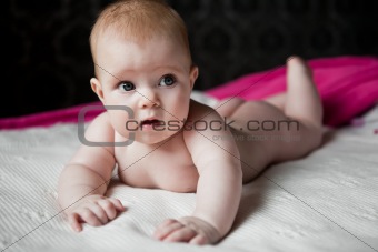 infant lying on a white rug, and surprised looks away
