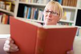 Happy senior woman with glasses reading book at home