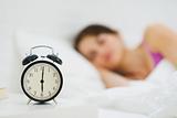 Alarm clock on table and woman sleeping in background
