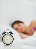 Alarm clock on table and woman sleeping in background