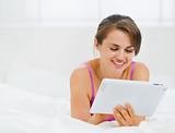 Smiling girl laying in bed and using tablet PC
