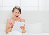 Surprised woman sitting in bed and using tablet PC
