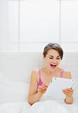 Surprised girl sitting in bed and using tablet PC