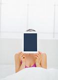 Girl sitting in bed and hiding tablet PC in front of face