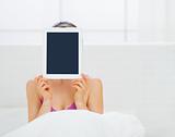 Woman sitting in bed and hiding tablet PC in front of face