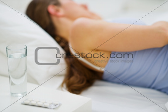 Closeup on pills and glass of water on table and sleeping girl in background