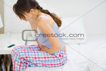 Girl with stomach ache sitting on bed