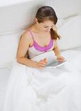 Woman sitting in bed and using tablet PC