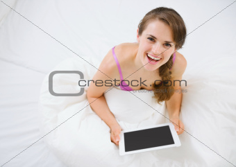 Smiling woman sitting in bed and using tablet PC