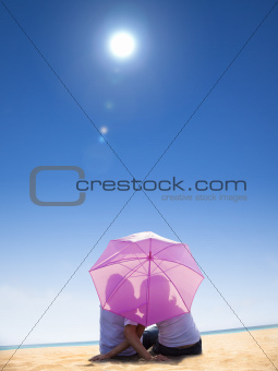 Couple kissing under umbrella on the beach