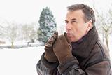 Senior Man Standing Outside In Snowy Landscape Warming Hands
